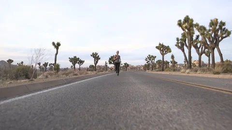 Female model running toward camera on desert road at sunset Stock Footage 76722748