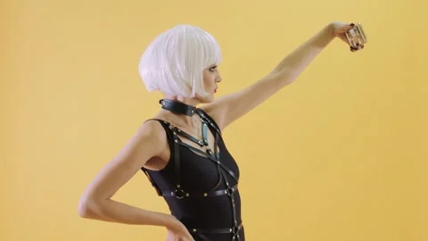 Female model sporting white wig, black harness top, posing with smartphone near Stock Footage 296702484
