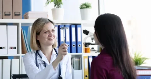 Female neurologist checking visual reflexes of nervous system using hammer in Stock Footage 194419016