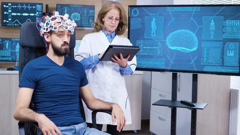 Female neurologist reading data from brainwave scanning headset Stock Footage 119653375