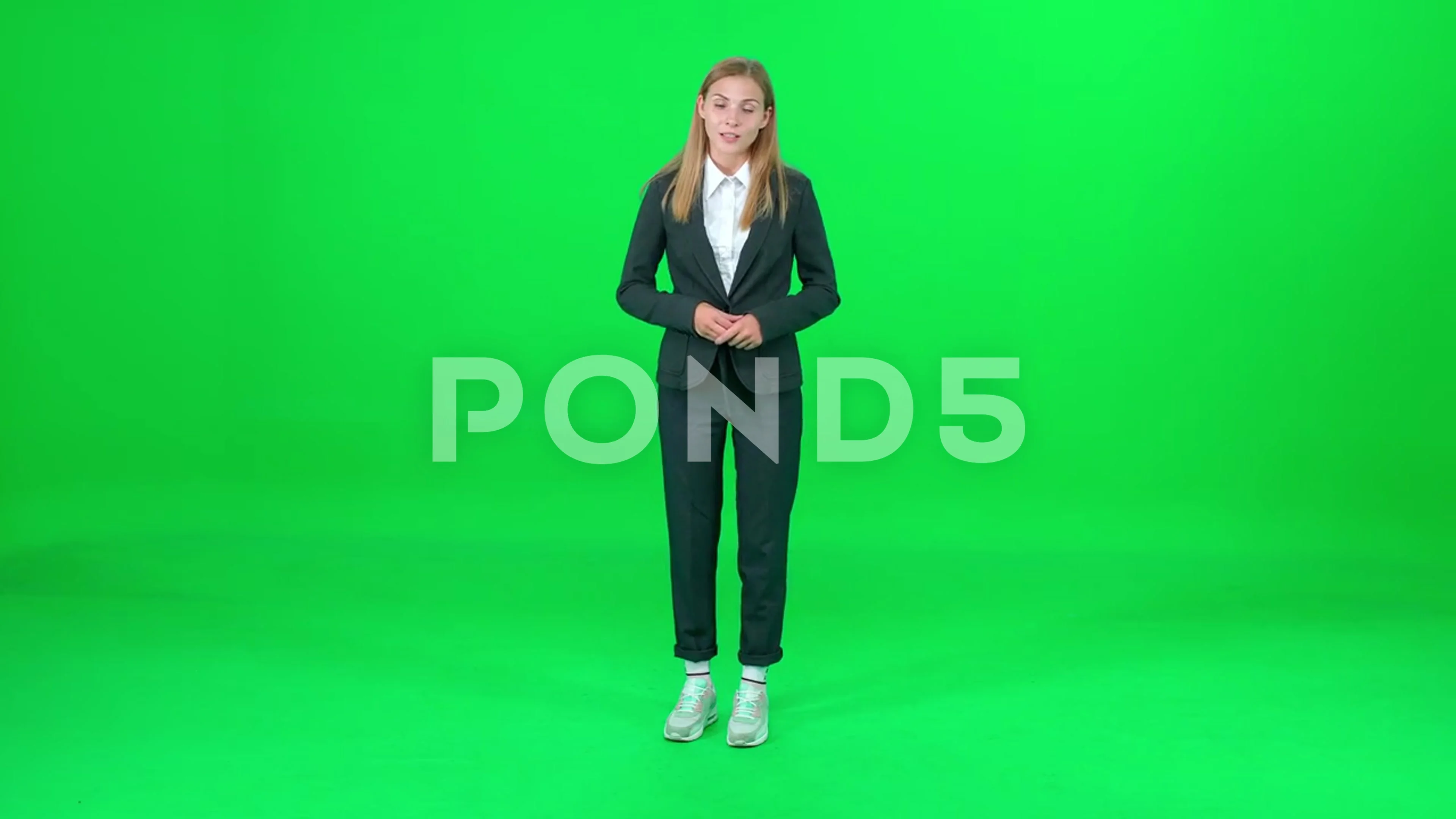 Female news reporter stands and speaks on a green background, looks into the