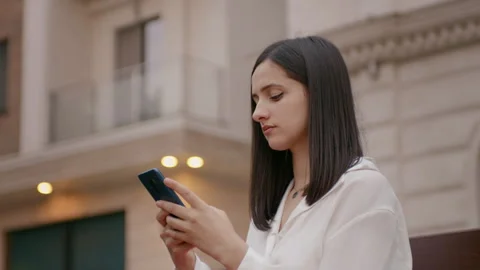 Female nodding while typing a message on smartphone in front of office building. Vídeos de archivo 295808843
