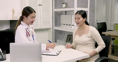 Female obstetrician taking notes while talking to Asian pregnant patient during 스톡 동영상 329658945