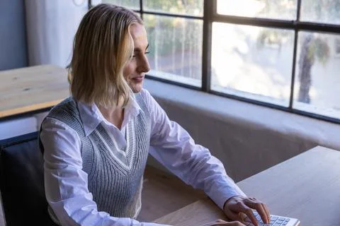Female office worker typing on wireless keyboard at desk by grid window in Stock Photos