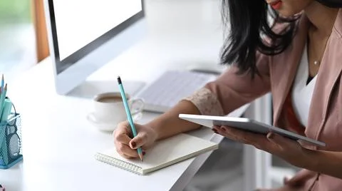 Female office worker using digital tablet and making notes on notebook. Stock Photos