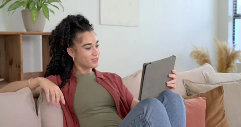 Female in olive top tapping tablet, smiling, reclining on sofa at home, reacting Stock Footage 345065226