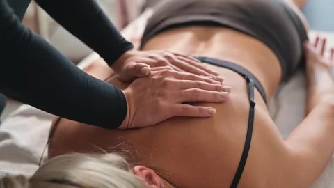 A female osteopath applies hands-on techniques to a patient's back, focusing on Vídeos de archivo 344377722