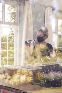 Female Owner Of Coffee Shop Wearing Face Mask Turning Round Open Sign During Stock Photos