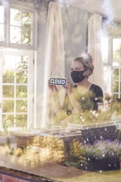 Female Owner Of Coffee Shop Wearing Face Mask Turning Round Closed Sign During Stock Photos