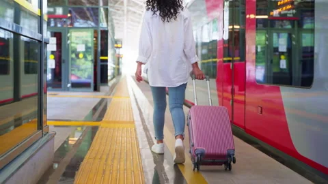 Female passenger with rolling suitcase walking along the station platform Stock Footage 232012207