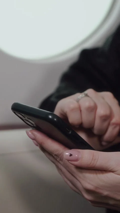 Female passenger using smartphone while seated by airplane window, engaged in 库存影片 329201829