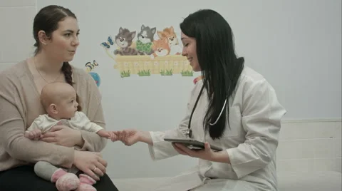 Female pediatrician doctor shows something on tablet  to woman with small baby Stock Footage