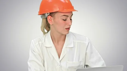 Female pensive architect using laptop and paper plan to check progress on white Vídeos de archivo 74218815
