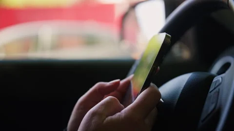 Female person texting on smartphone while sitting behind steering wheel, di.. Stockbeeldmateriaal 333835627