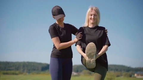 Female personal trainer helping a client stretch her leg outdoors Video stock 331515353