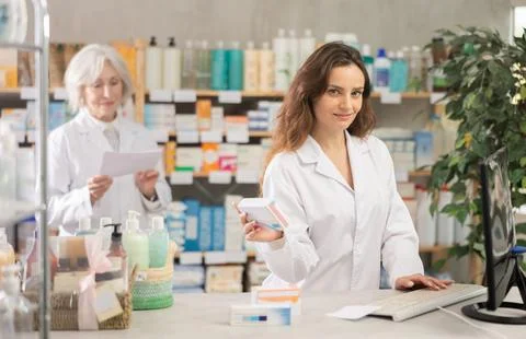 Female pharmacist using computer, companion at background 库存照片