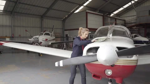 Female pilot in the hangar doing maintenance on a plane's engine, checking oi 库存影片 146376319