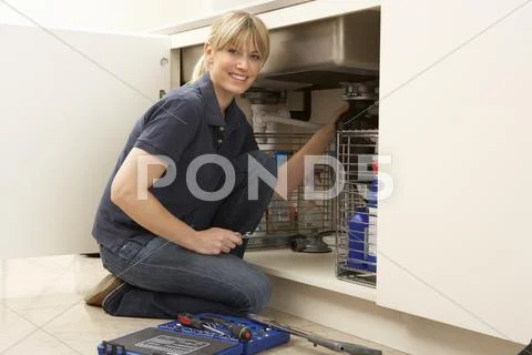 Female Plumber Working On Sink In Kitchen Stock Photos