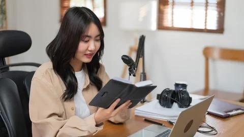 Female podcaster reading script in notebook and speaking content to making .. Stock Photos