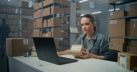 Female post office worker scans cardboard parcel using barcode scanner, enters Stock Footage 307616604
