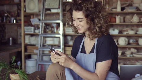 Female potter using mobile phone in her art studio Stock Footage 161802245