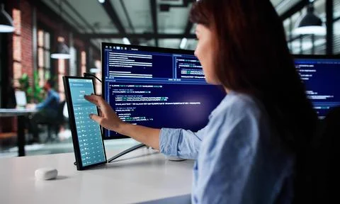 Female Programmer Analyzing Weather Patterns On Secondary Computer Screen Foto stock