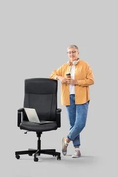 Female programmer with coffee and laptop on chair against light background Foto stock