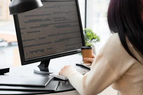 Female programmer with coffee cup testing code on computer in office, back vi Foto stock