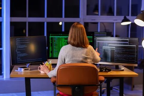 Female programmer with cup of coffee and computers working in office at night Stock-Fotos