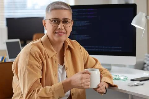 Female programmer with cup of coffee at desk in office Stock Photos