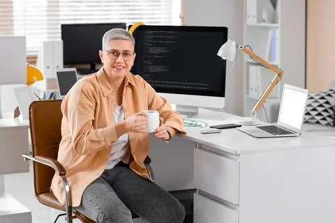 Female programmer with cup of coffee at desk in office Stock-Fotos