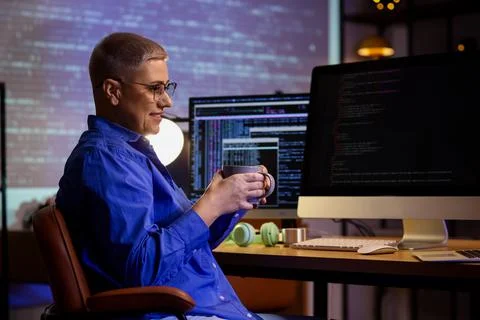 Female programmer with cup of coffee sitting in office at night Stock-Fotos
