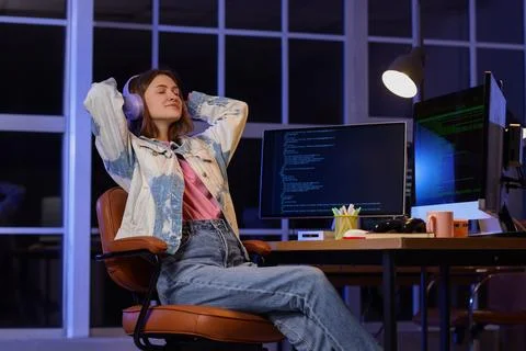 Female programmer with headphones and computers relaxing in office at night Stock-Fotos