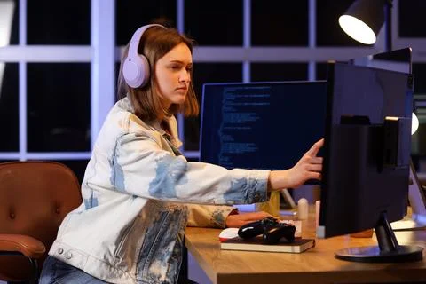 Female programmer with headphones and computers working in office at night Stock Photos
