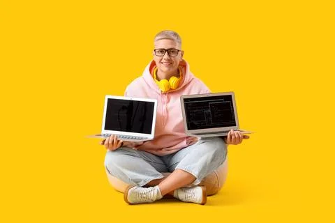 Female programmer with laptops in beanbag on yellow background Stock Photos