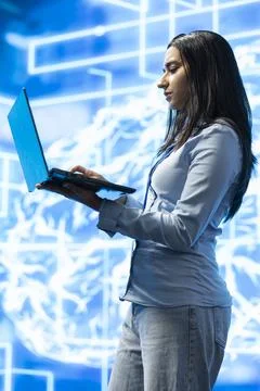 Female programmer types on laptop while standing next to AI visualization Stock Photos