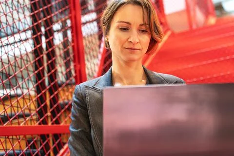 Female programmer working on code in modern office with industrial red stairs 库存照片