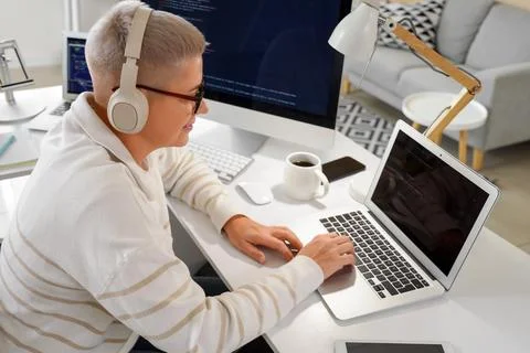 Female programmer working with headphones and laptop at desk in office Stock-Fotos