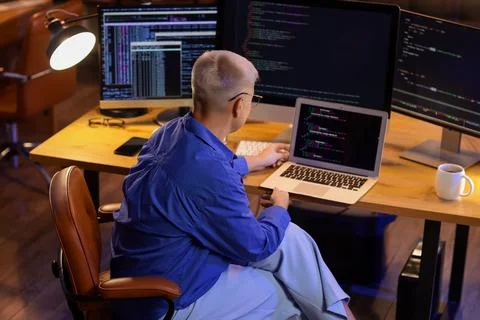 Female programmer working with laptop in office at night, back view Stock Photos