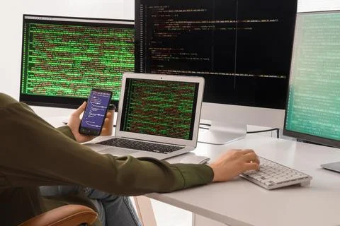 Female programmer working with mobile phone and computer at desk in office Stock Photos