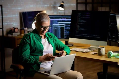 Female programmer working with mobile phone and laptop in office at night Stock Photos