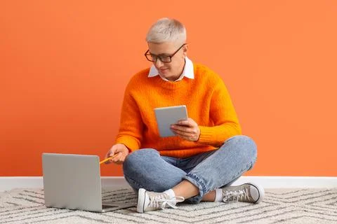 Female programmer working with tablet computer and laptop near orange wall Stock-Fotos