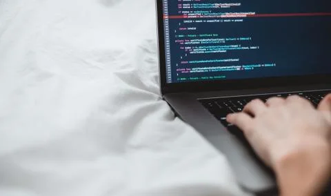 Female programmer writes program code on a computer laptop in the bed . 库存照片
