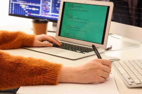 Female programmer's hands working with laptop and notebook on table in office Stock Photos