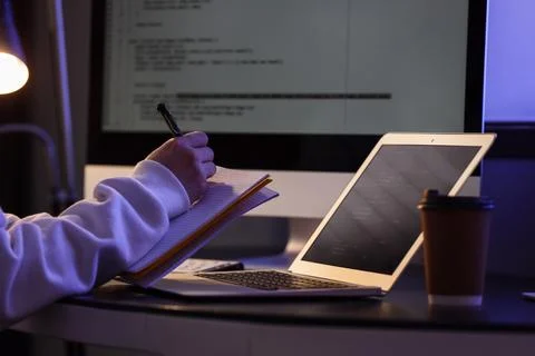 Female programmer's hands writing on notebook in dark office at night Stock-Fotos
