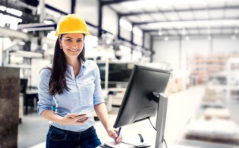 Female project manager standing by computrer in modern industrial factory Stockfoto's