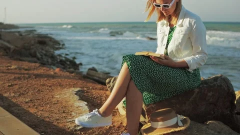Female reader sitting on coastal boulder, absorbed in book, wearing white j.. Stock Footage 310123248