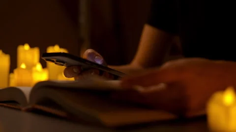 Female reading book and using typing smartphone sitting at table in candlelit Stock Footage 296270906