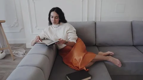 Female reading book while sitting on couch Stock Footage 259837717