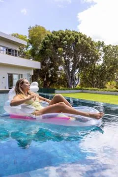 Female reclining on clear float with pink headrest, wearing light swimsuit in Stock Photos